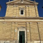 Facciata della Basilica di Sant’Anastasia al Palatino a Roma, illuminata dal sole del mattino, con la scritta “Adoremus” sopra il portale principale.