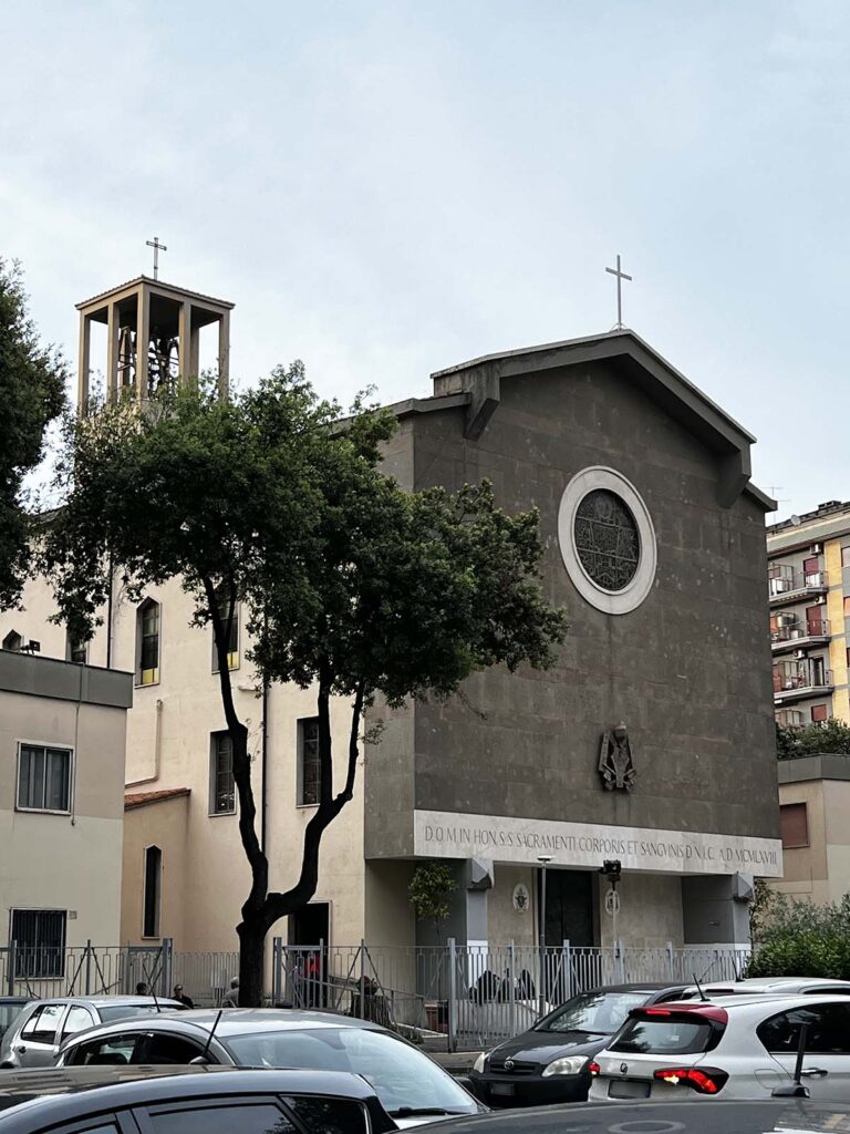 Facciata della chiesa del SS. Sacramento a Tor de' Schiavi, Roma, con campanile, alberi e traffico urbano in primo piano.