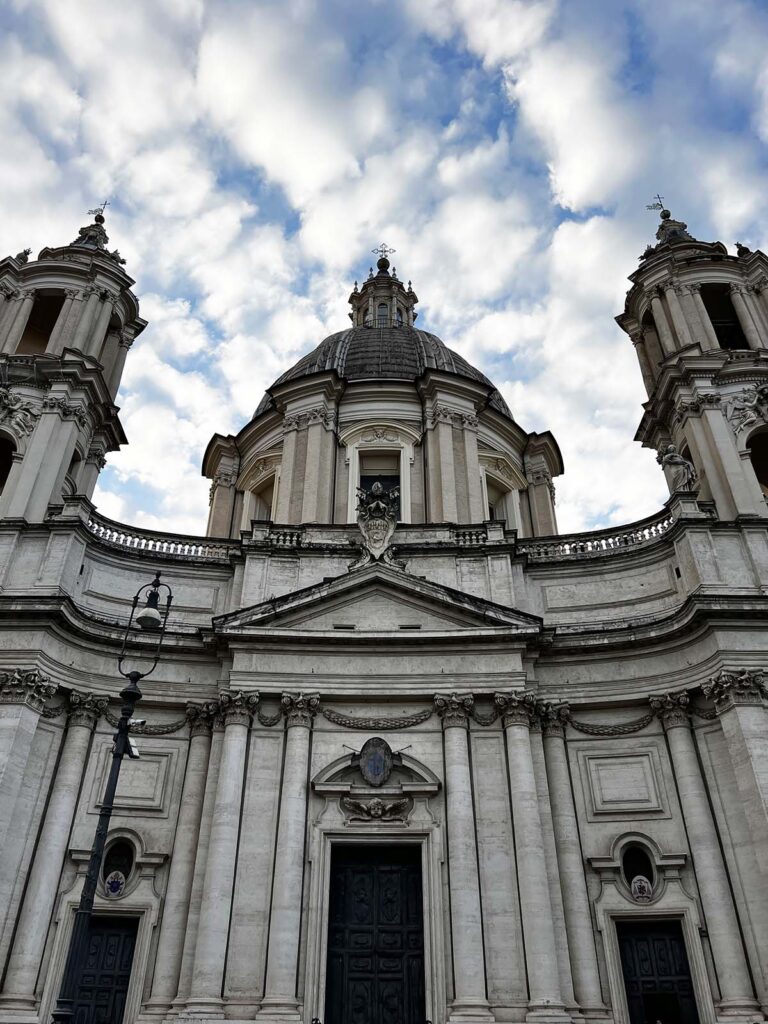 Facciata barocca della chiesa di Sant’Agnese in Agone a Roma vista dal basso con cielo nuvoloso.