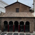 Facciata semplice e antica della chiesa di San Vitale al Quirinale vista dalle scale, con una persona sul sagrato.