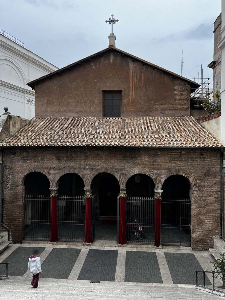 Facciata semplice e antica della chiesa di San Vitale al Quirinale vista dalle scale, con una persona sul sagrato.