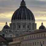 Cupola della Basilica di San Pietro illuminata dalla luce del tramonto con edifici in primo piano.